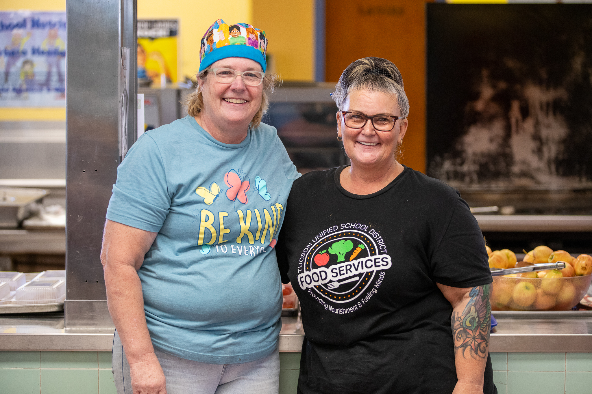 Two Food Services employees smile as they pose together in the cafeteria