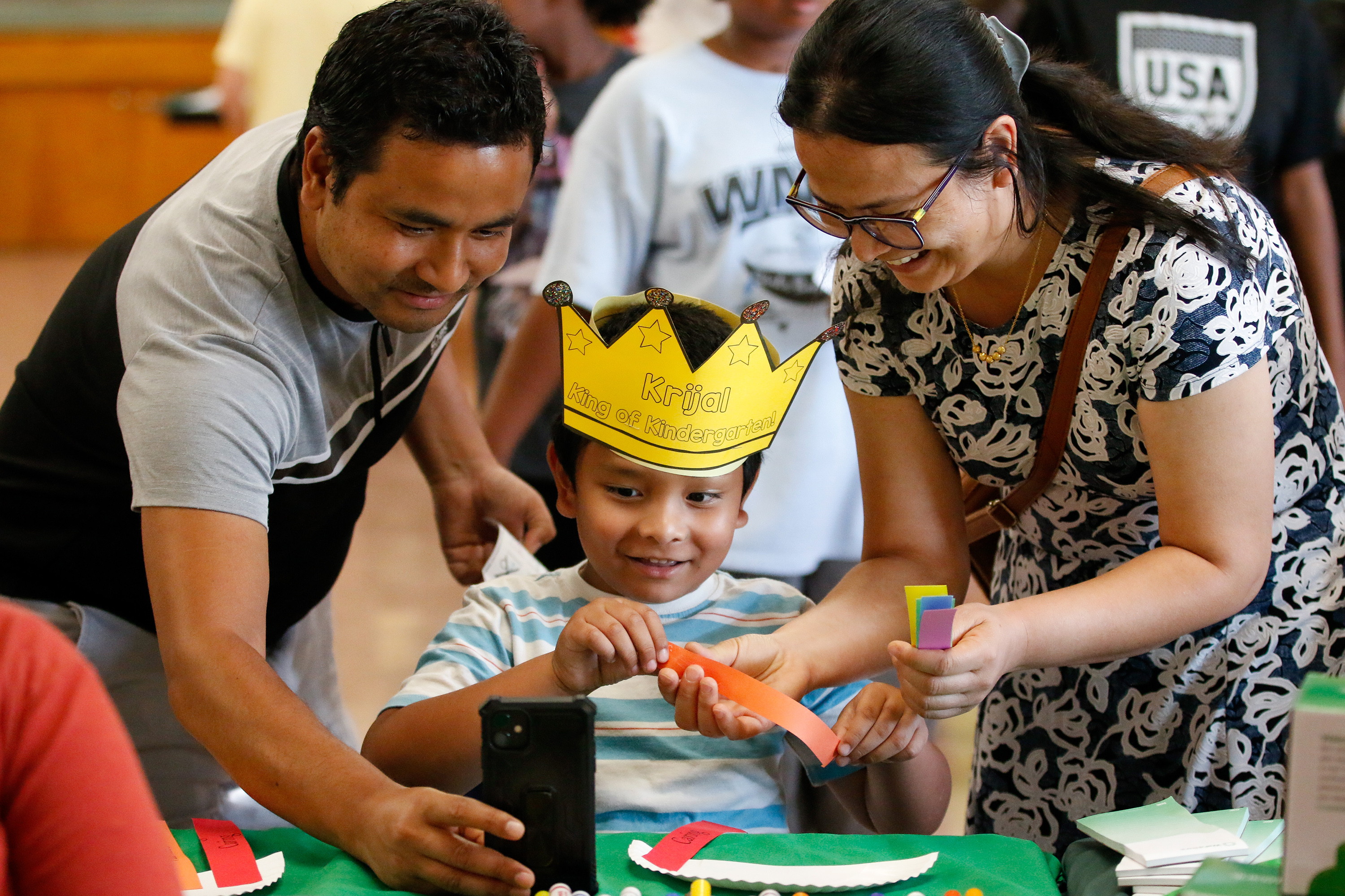 A little boy wearing a paper crown works on a craft with colored strips of paper