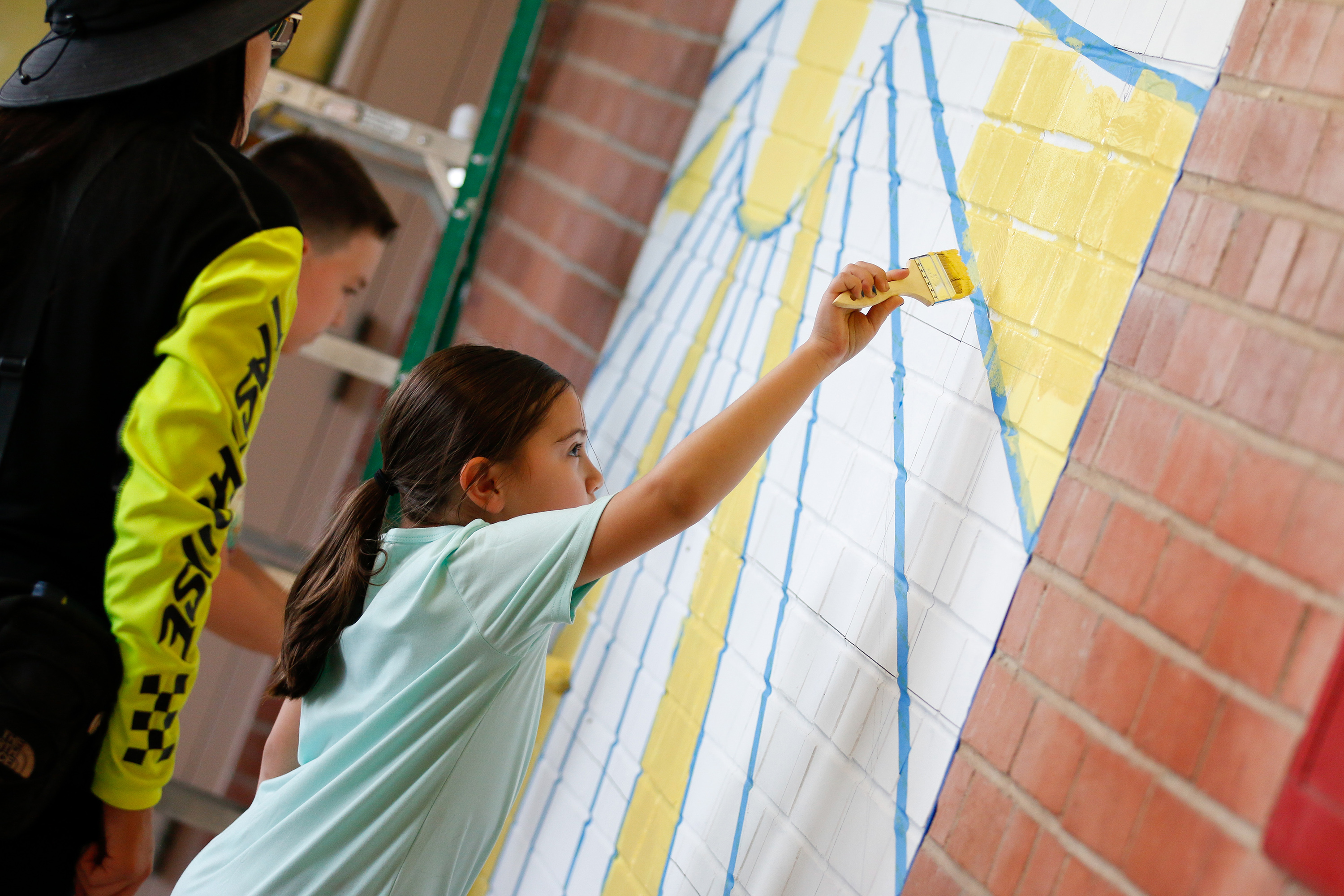 A little girl helps paint a sun mural on the wall