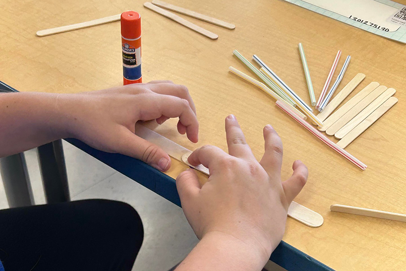 A closeup of hands gluing a popsicle stick