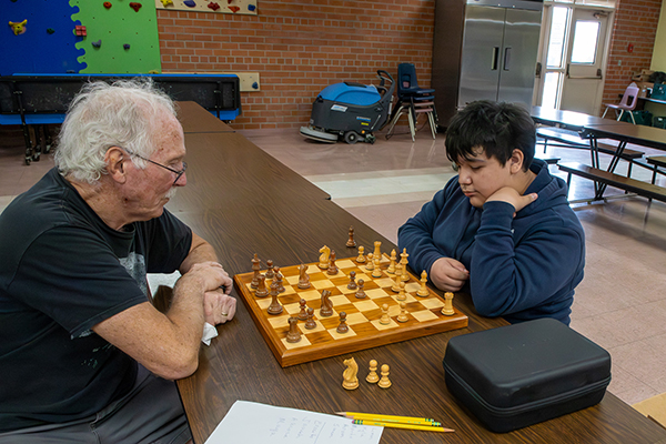 An older man and a young boy play chess together