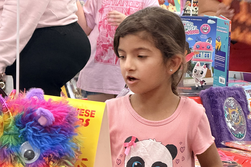 A girl in a pink shirt looks at a colorful stuffed animal