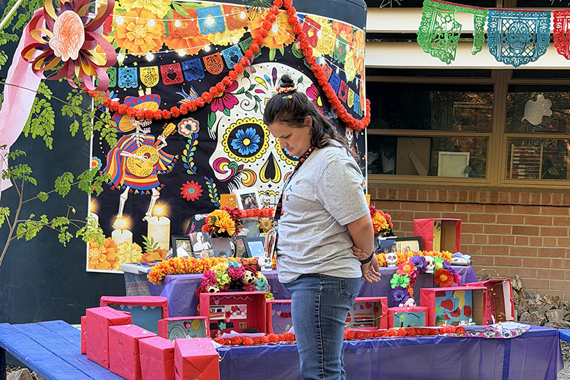 A woman looks at an art display, with a colorful Dia de los Muertos scene behind her