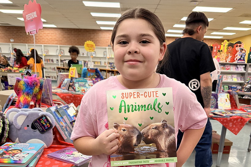 A little girl in a pink shirt holds up a Super-Cute Animals book