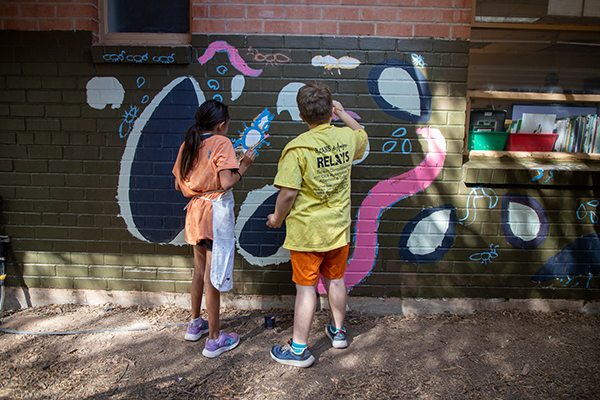 A girl and boy help paint a mural on the side of the school
