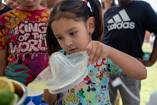 A little girl pours juice into her cup from a juicer