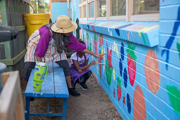 A woman and a little girl paint a mural on the side of the school