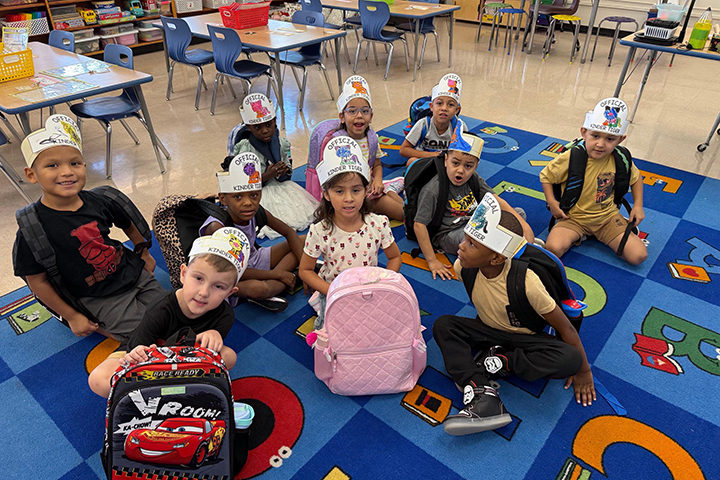 Students wearing paper crowns sit on a rug in a classroom