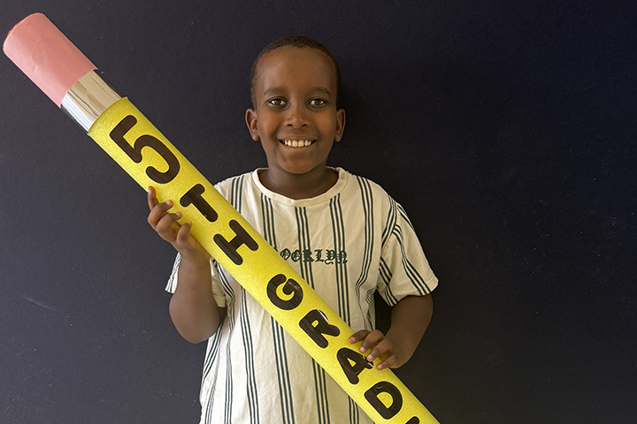 A boy holds a giant pencil with the words 5th Grade