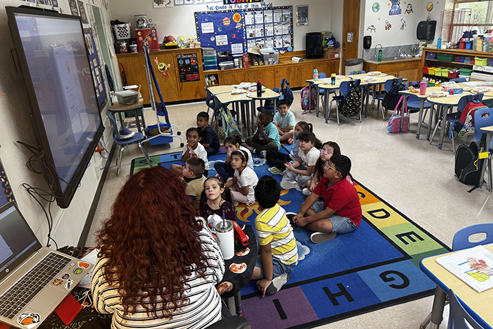 Students sitting on a rug listen to their teacher