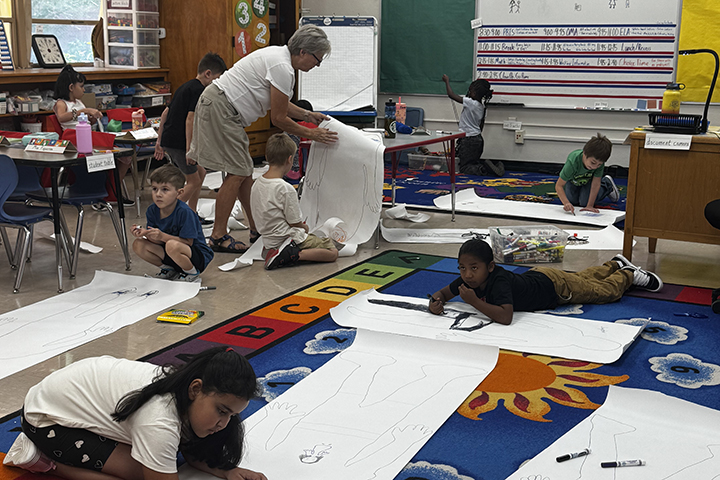 Students draw on large pieces of paper on the floor