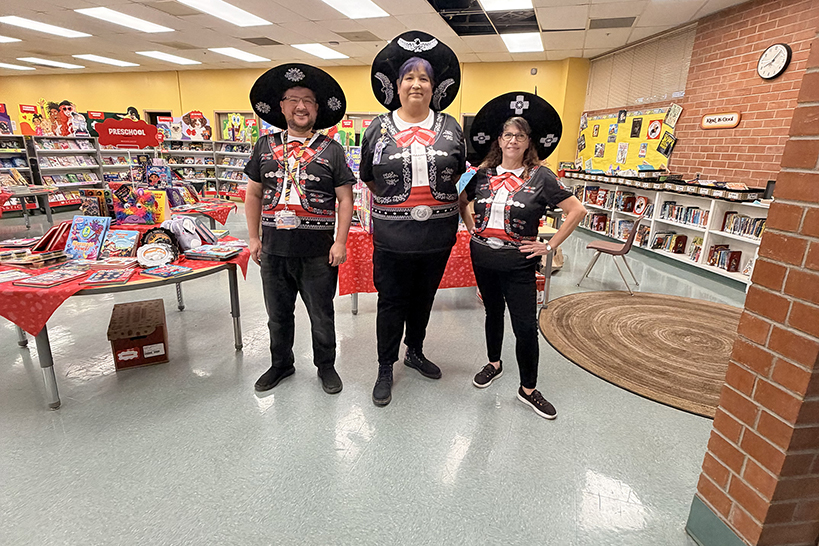 Three teachers dressed in mariachi costumes stand in the library
