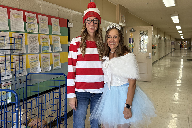 A woman dressed as Where's Waldo and a woman dressed as the Tooth Fairy stand in the hallway
