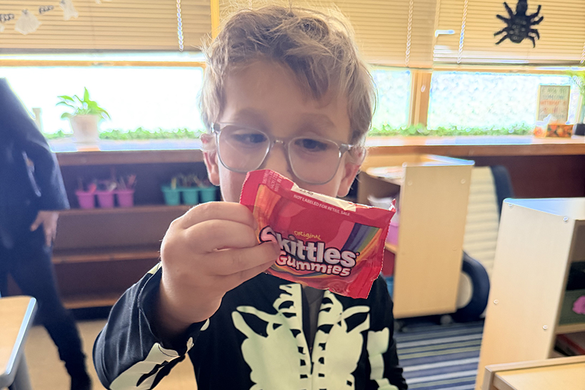 A little boy in a skeleton costume holds up a package of Skittles gummies