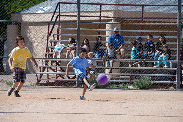 A boy in a blue shirt kicks the purple kickball