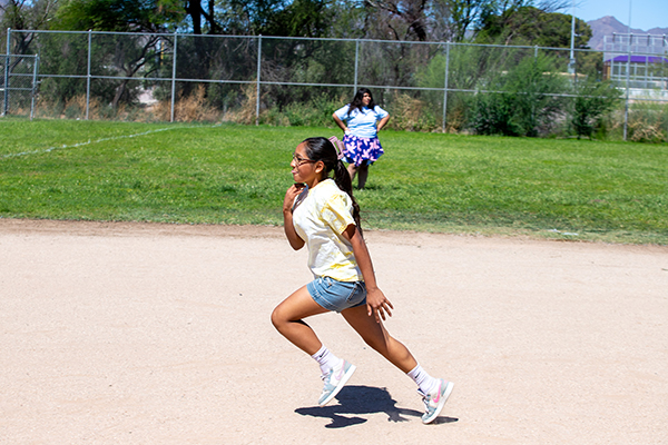 A girl in a yellow shirt sticks out her tongue as she runs around the field