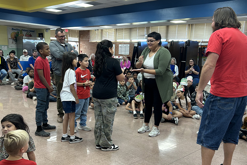 A group of students stand in the cafeteria, with two adults nearby