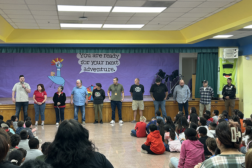 A group of people lined up in front of the stage, with students sitting on the floor watching